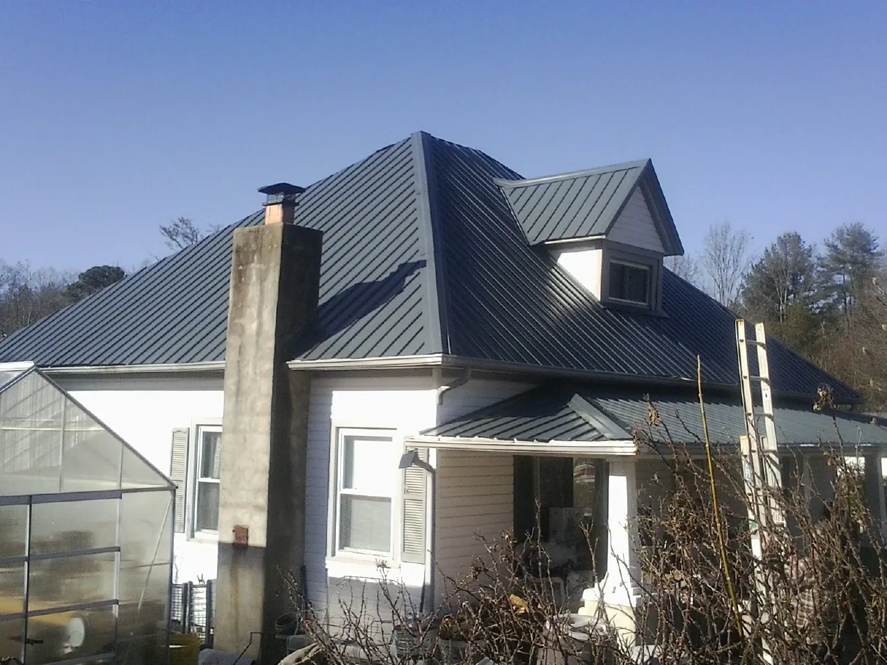 Dark blue standing seam metal roof on a white farmhouse with dormer — Slate & Tile Roof Repair by Roofing Brothers in Waconia
