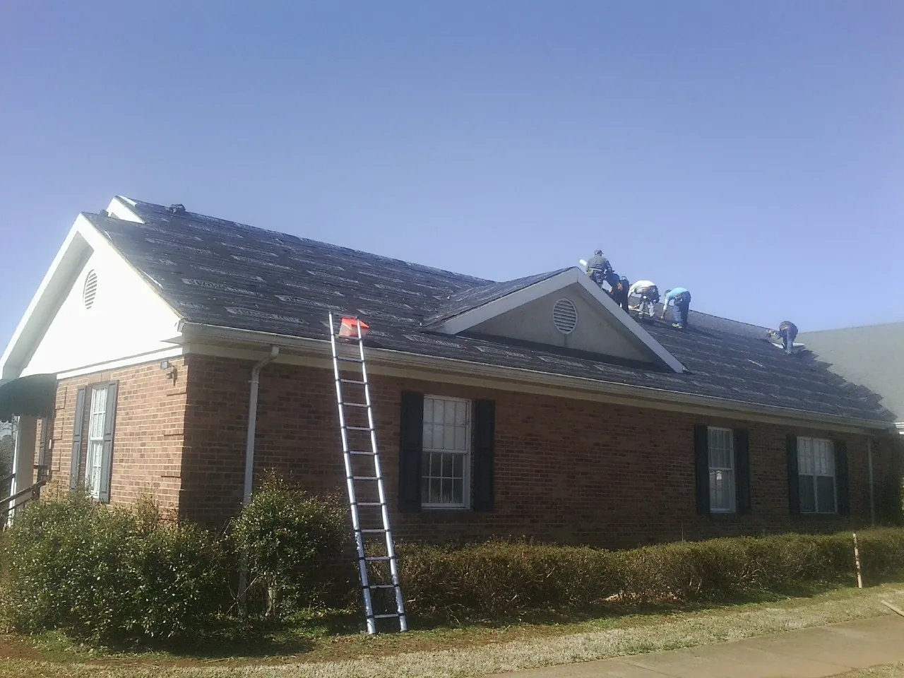 Crew tearing shingles off a brick ranch roof with a ladder set — Emergency Roof Repair work by our crew in Waconia