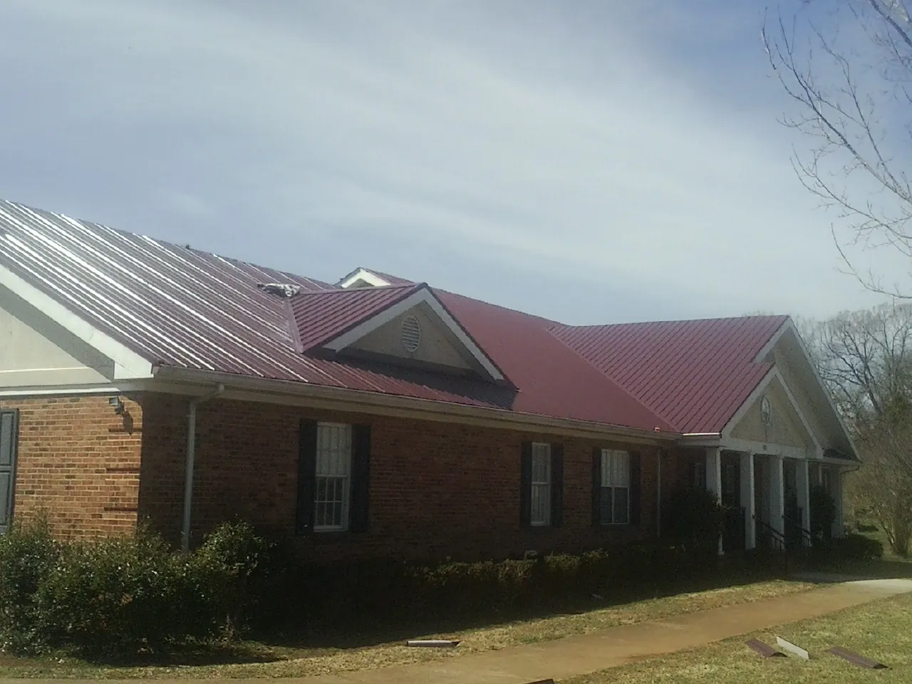 Red metal roof with gabled entries on a long brick building, from a Hail Damage Roof Repair job in Waconia