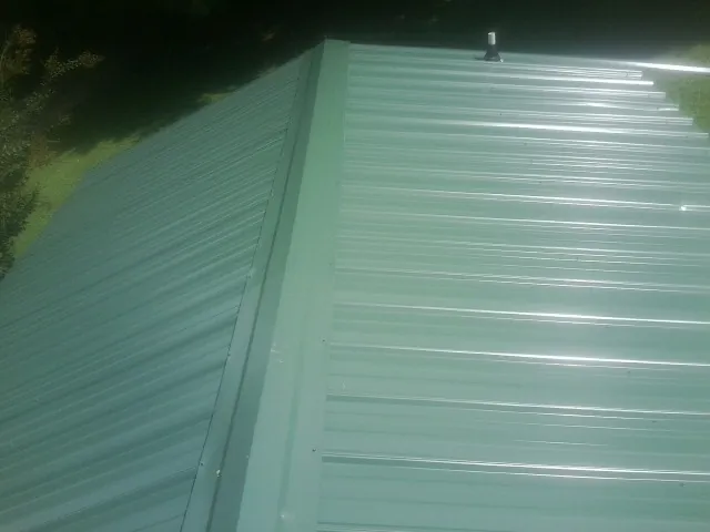 New green metal panels meeting at the ridge of a roof — Flat Roof Repair work by our crew in Waconia