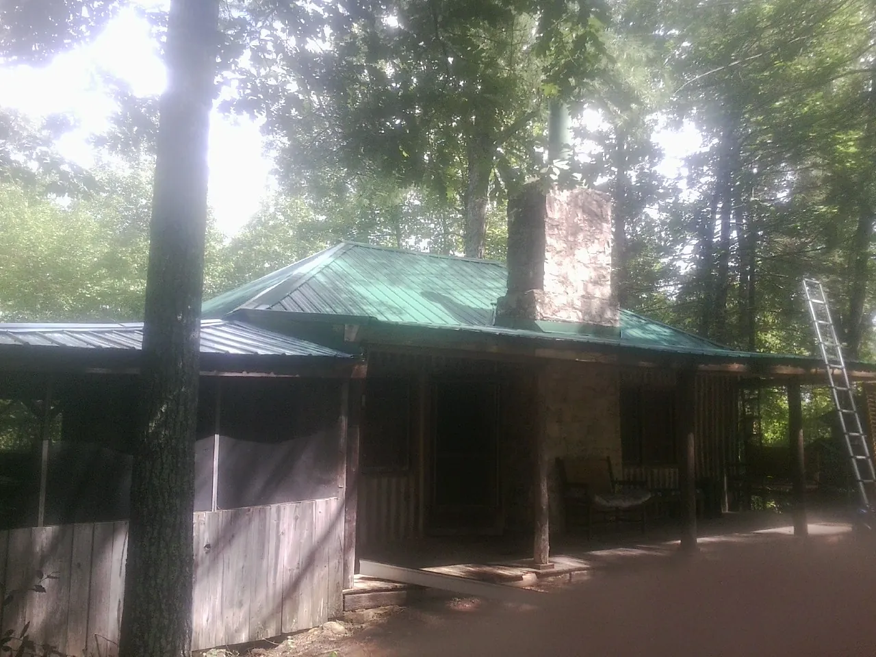 Green metal roof and stone chimney above a log cabin porch in Waconia