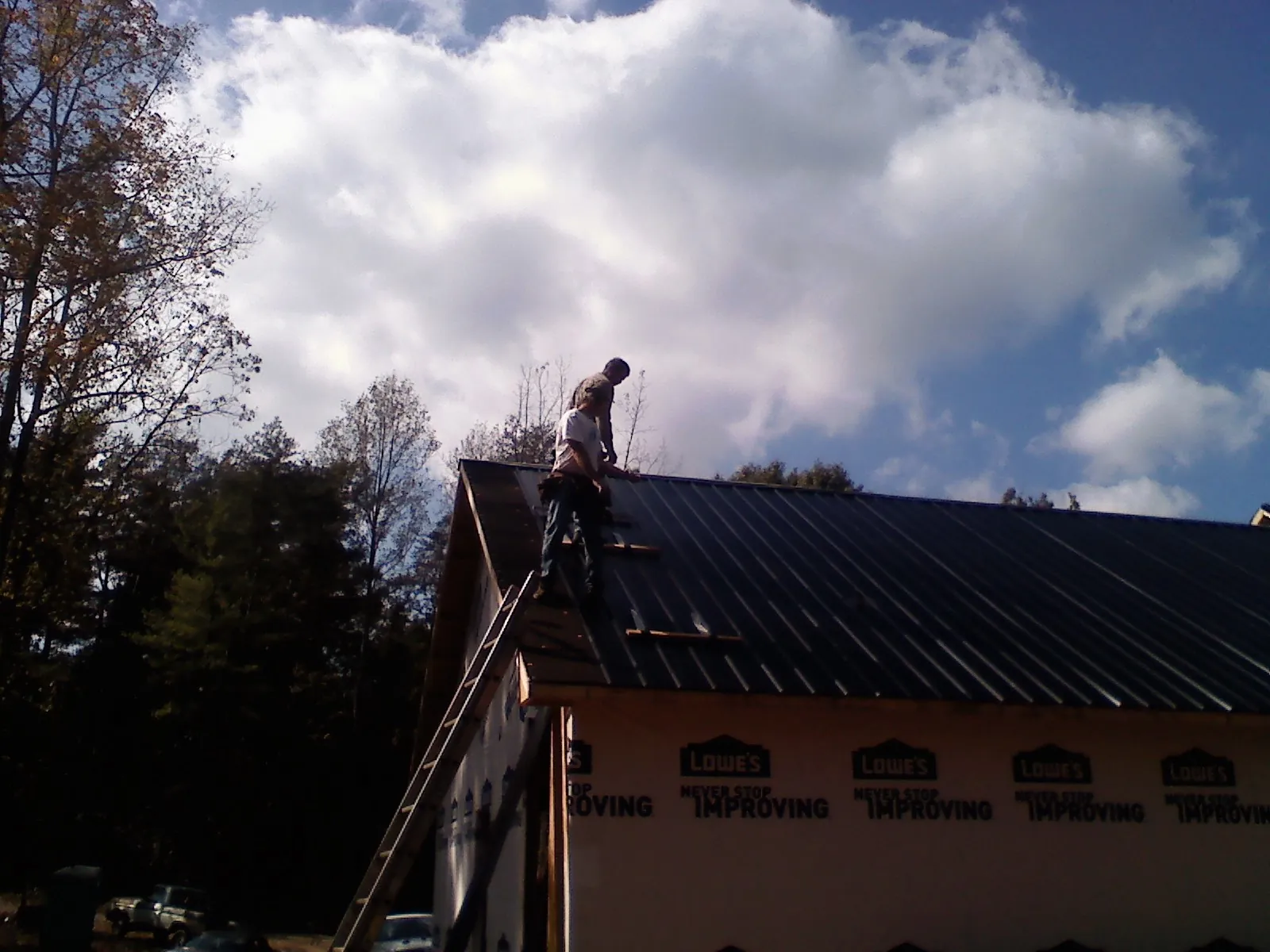 Roofer fastening dark metal panels high against a cloudy sky, from a Roof Inspection job in Waconia
