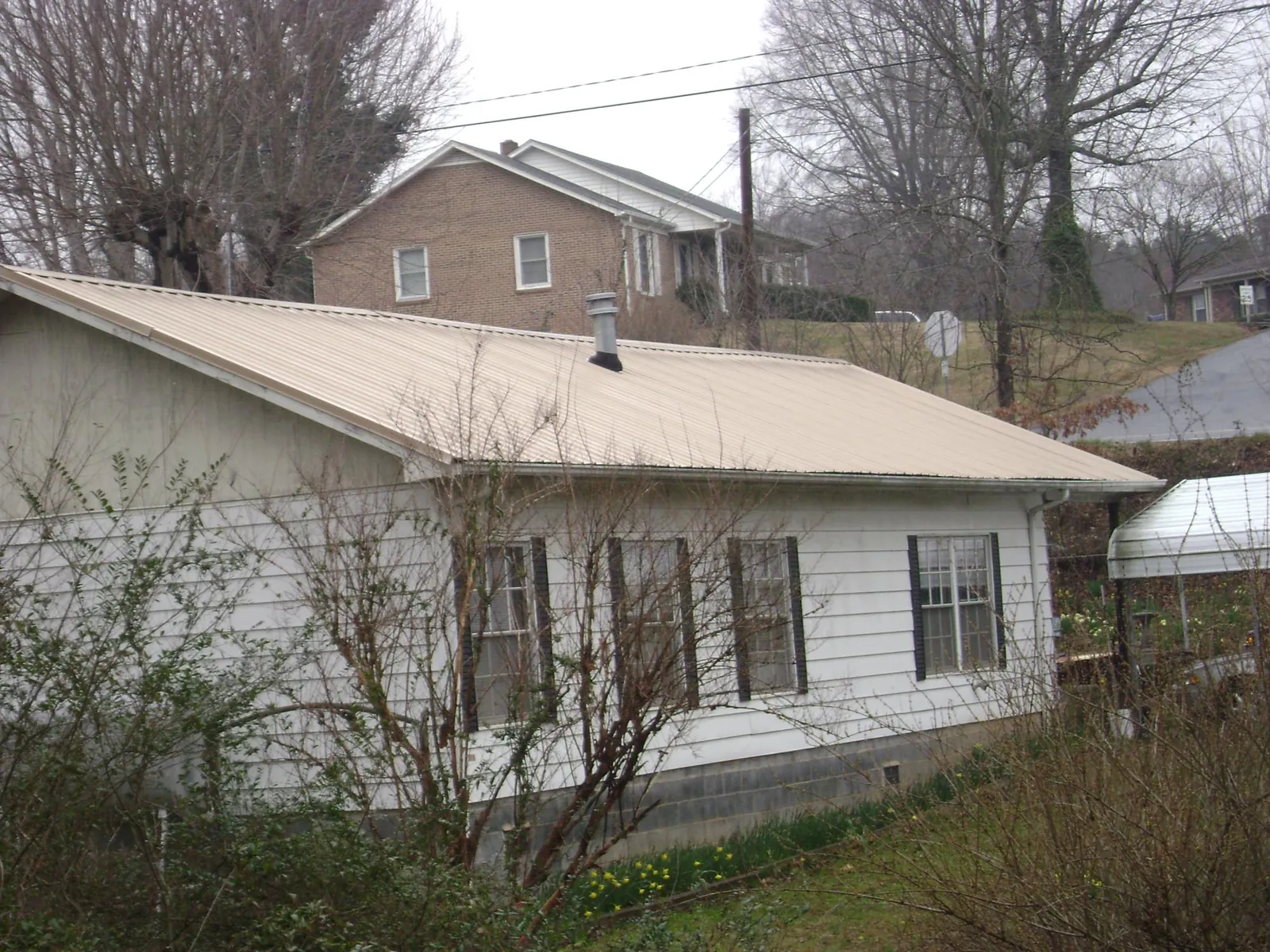 Tan metal roof on a white sided house set into a hillside — Commercial Roofing by Roofing Brothers in Waconia